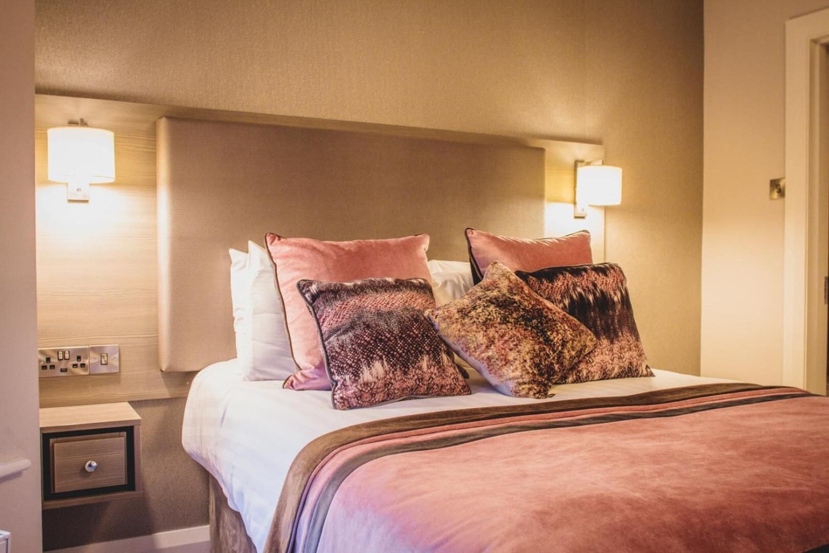 Una habitación de hotel con una cama, dos lámparas de noche, una mesita de noche y un enchufe.