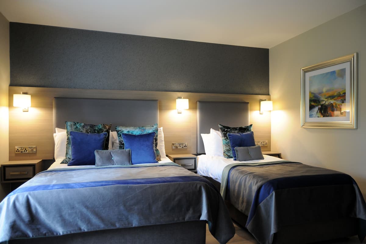 Quarto de hotel com duas camas, cada uma com cabeceira, abajures e um quadro na parede.