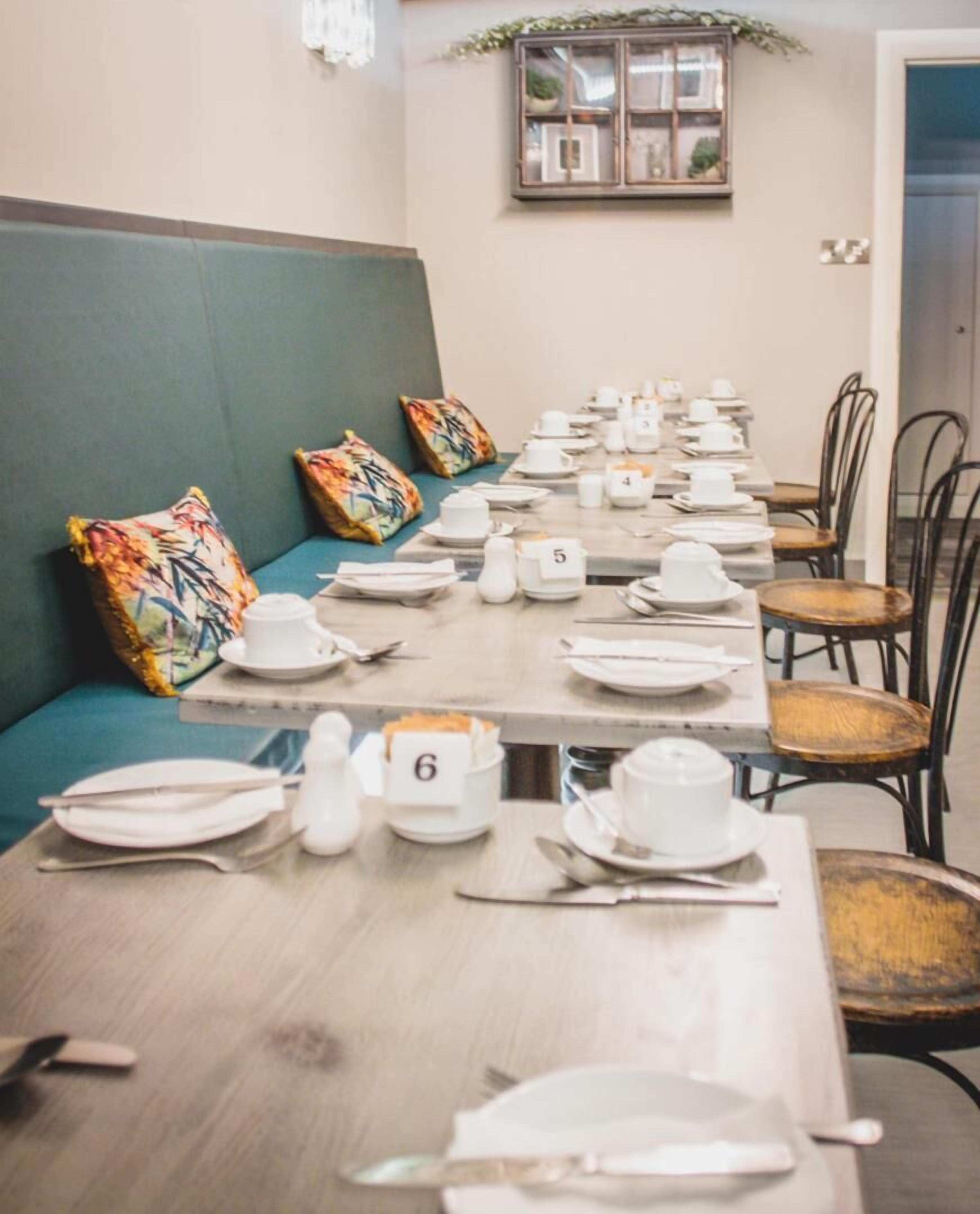 Uma sala de jantar com uma mesa comprida posta para refeição, assentos numerados e um banco estofado verde.