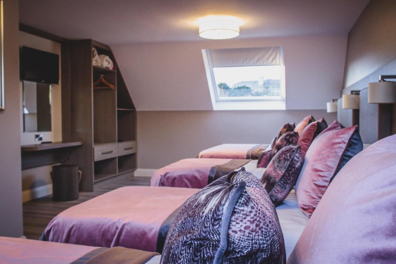 A bedroom with two beds, a wardrobe, a desk, and a window with a view.