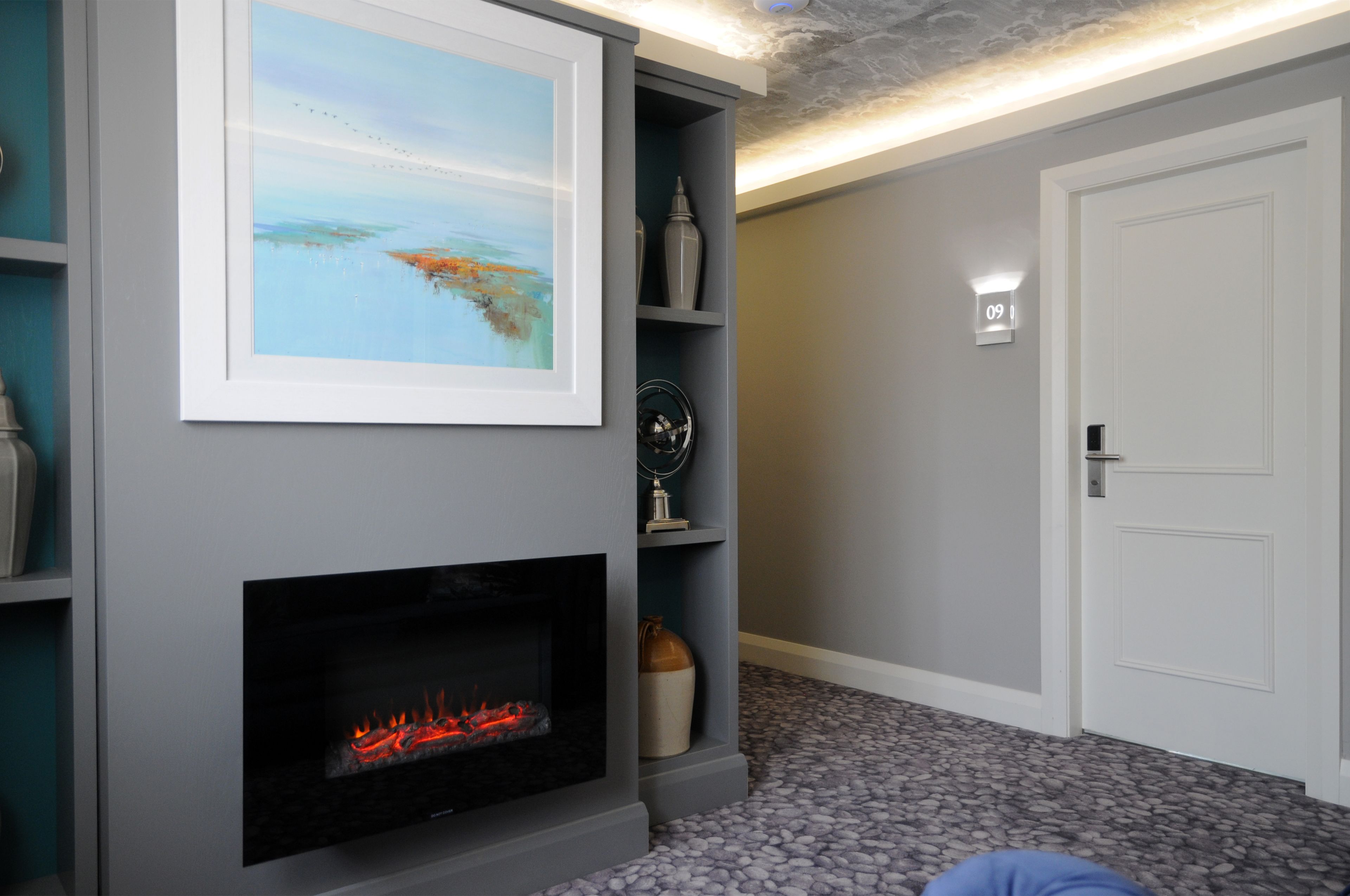 A room with a fireplace, a framed painting, and a door with a light above it.