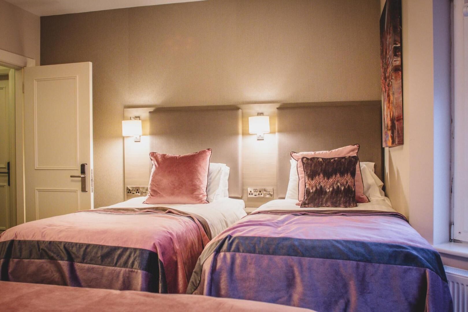 Two double beds with headboards, bedside lamps, and a door to the left.