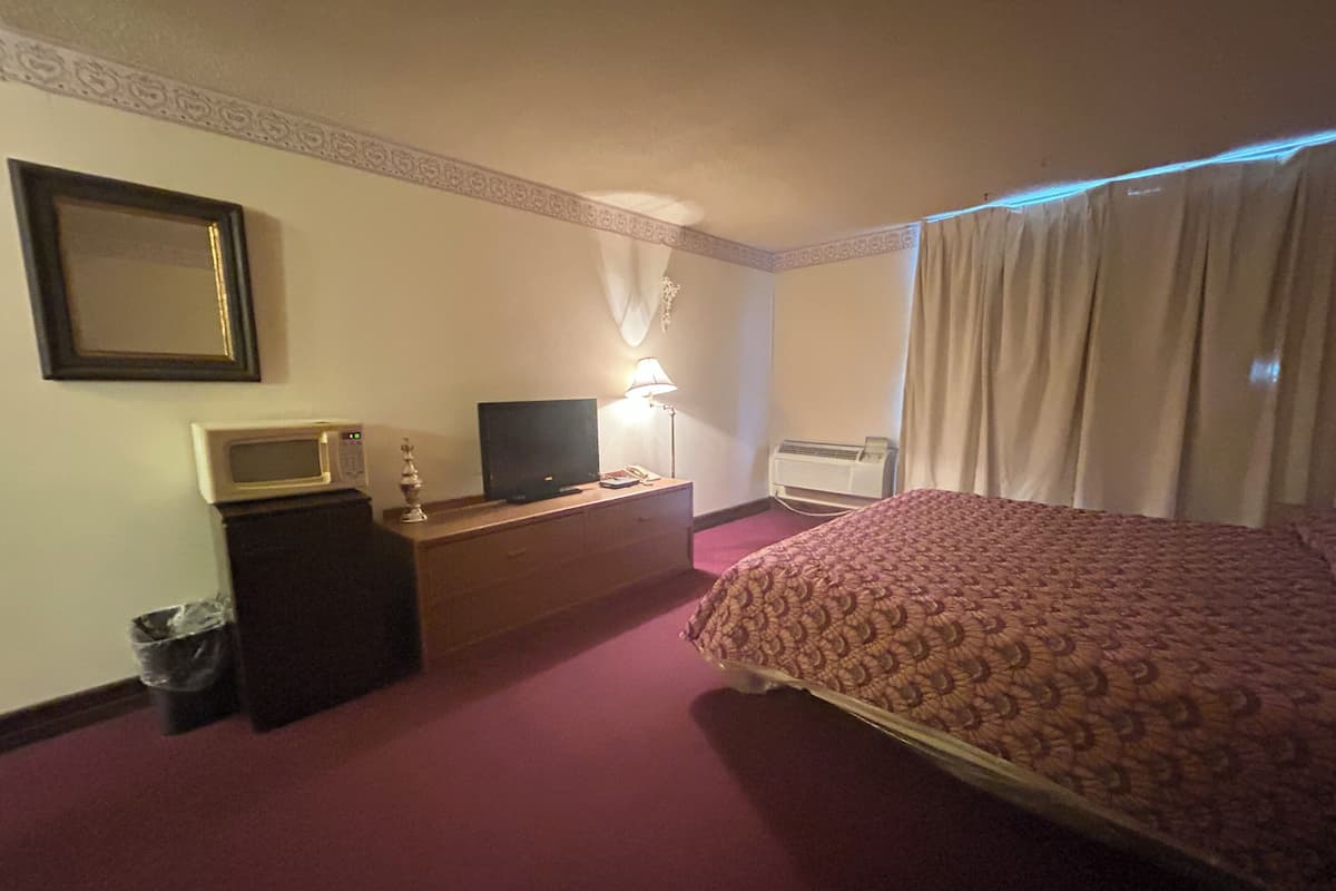 A hotel room with a bed, a desk with a television, a lamp, an air conditioner, and a trash bin.