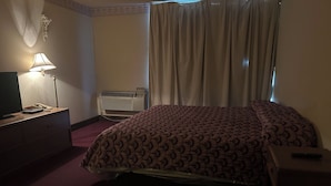 A hotel room with a bed, a desk with a lamp, a telephone, and an air conditioning unit. - Candlelight Inn by Capital O Scottsbluff (Scottsbluff)