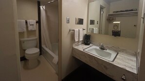 A bathroom with a toilet, a shower, a sink, and a mirror. - Candlelight Inn by Capital O Scottsbluff (Scottsbluff)