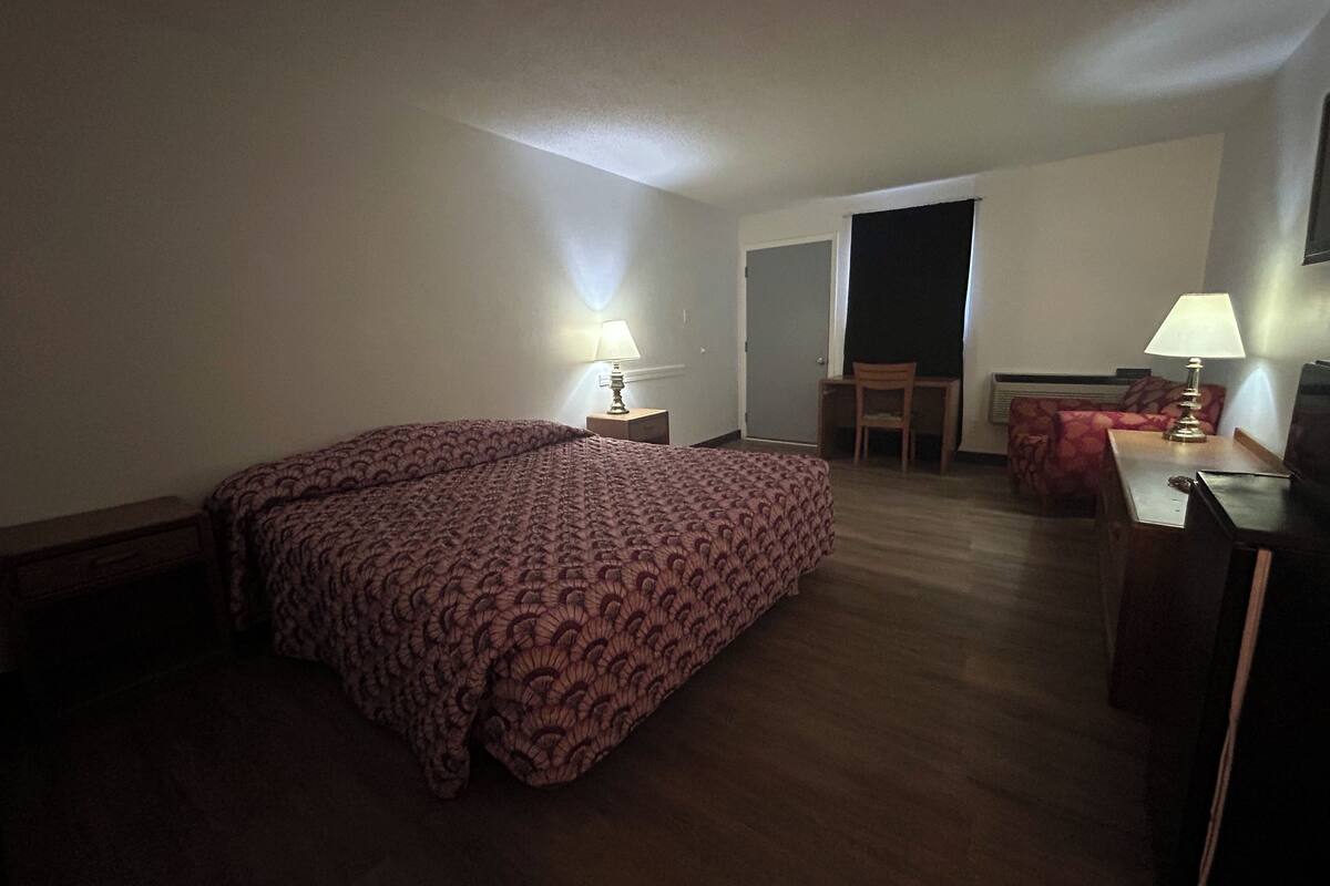 A hotel room with a large bed, a desk, a chair, and a lamp.