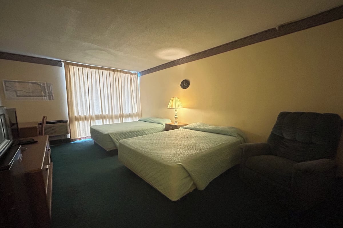 A hotel room with two beds, a desk with a computer, a chair, and a lamp.