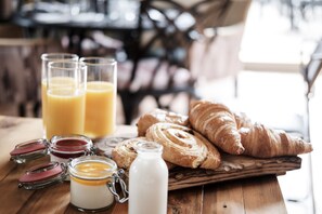 En frukostuppsättning med croissanter, en flaska mjölk och två glas apelsinjuice på ett träbord.