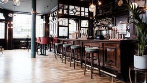 A bar area with wooden flooring, bar stools, and a bar counter with taps and bottles. - Half Moon (London)