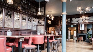 A bar area with wooden paneling, red bar stools, and hanging pendant lights. - Half Moon (London)