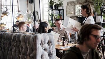 A restaurant interior with a tufted sofa, dining tables, and potted plants.