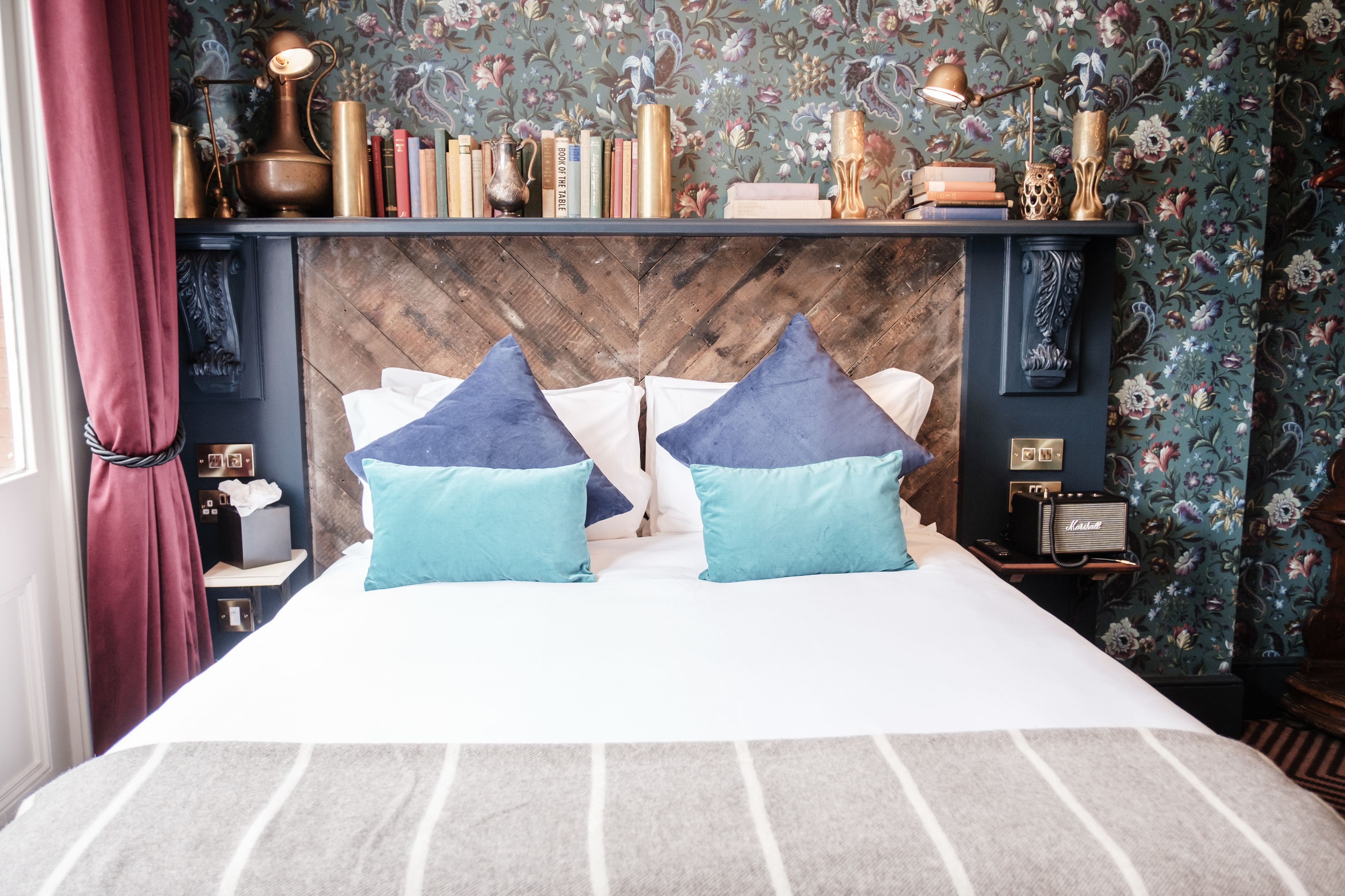 A bedroom with a bed, pillows, a nightstand, a lamp, and a bookshelf.