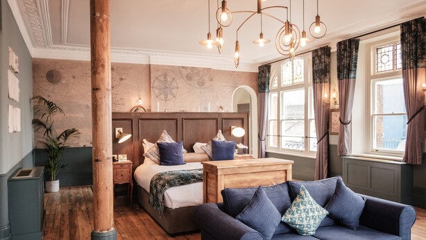 A cozy bedroom with a wooden headboard, a large bed with blue bedding, a blue sofa with patterned cushions, and a wooden floor. - Half Moon (London)