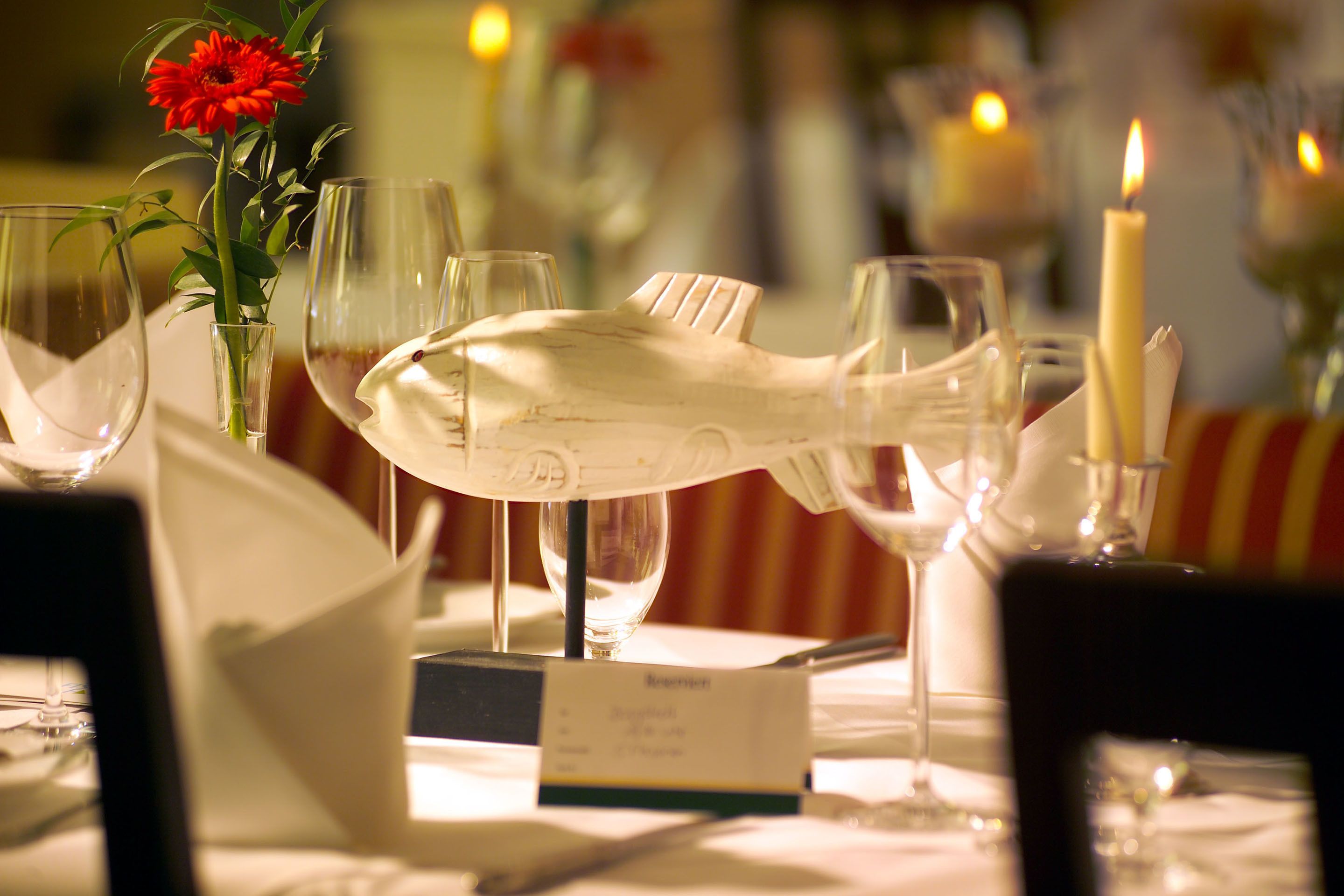 A dining table with a white fish-shaped centerpiece, wine glasses, and a candle.