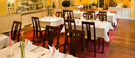 Un restaurante con varias mesas dispuestas para comer, una zona de cocina y una alfombra roja que lleva al área de asientos.
