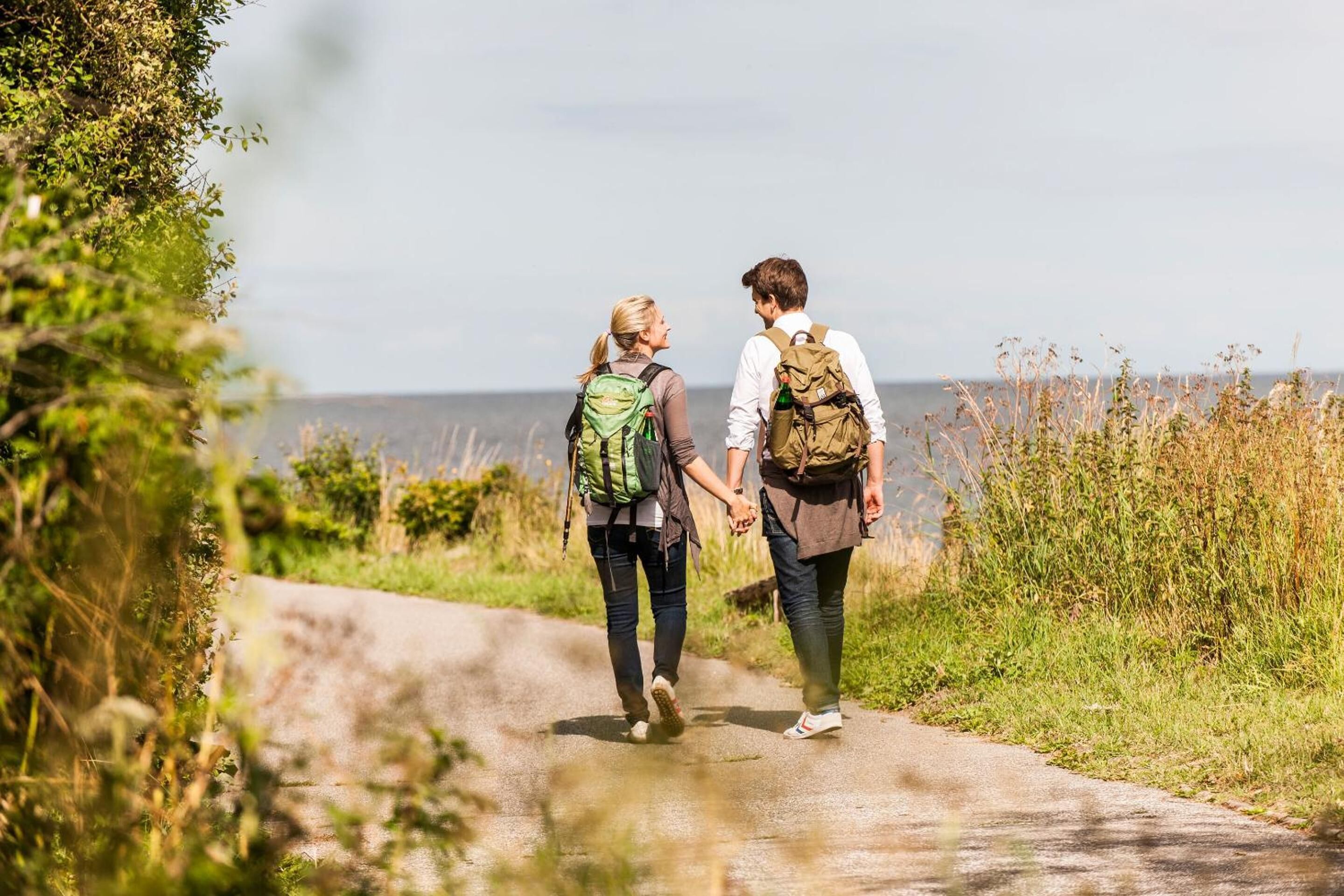 Two people walking on a paved path surrounded by greenery.