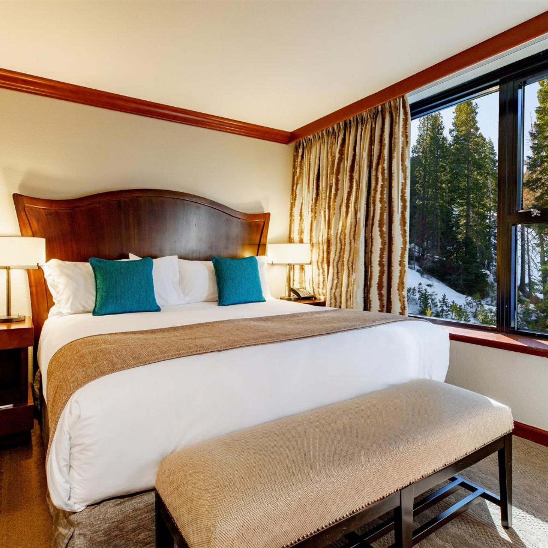 A hotel room with a large bed, a bench, a nightstand, and a window with curtains.