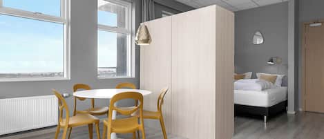 Una habitación moderna con una mesa redonda y sillas, una cama, y vistas a través de amplios ventanales.