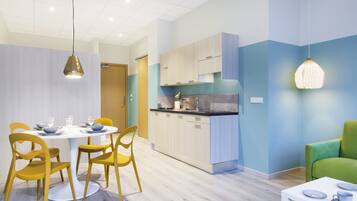 Une cuisine moderne avec des meubles de couleur bois clair, un îlot central et un coin repas agrémenté de chaises jaunes et d’une table blanche.