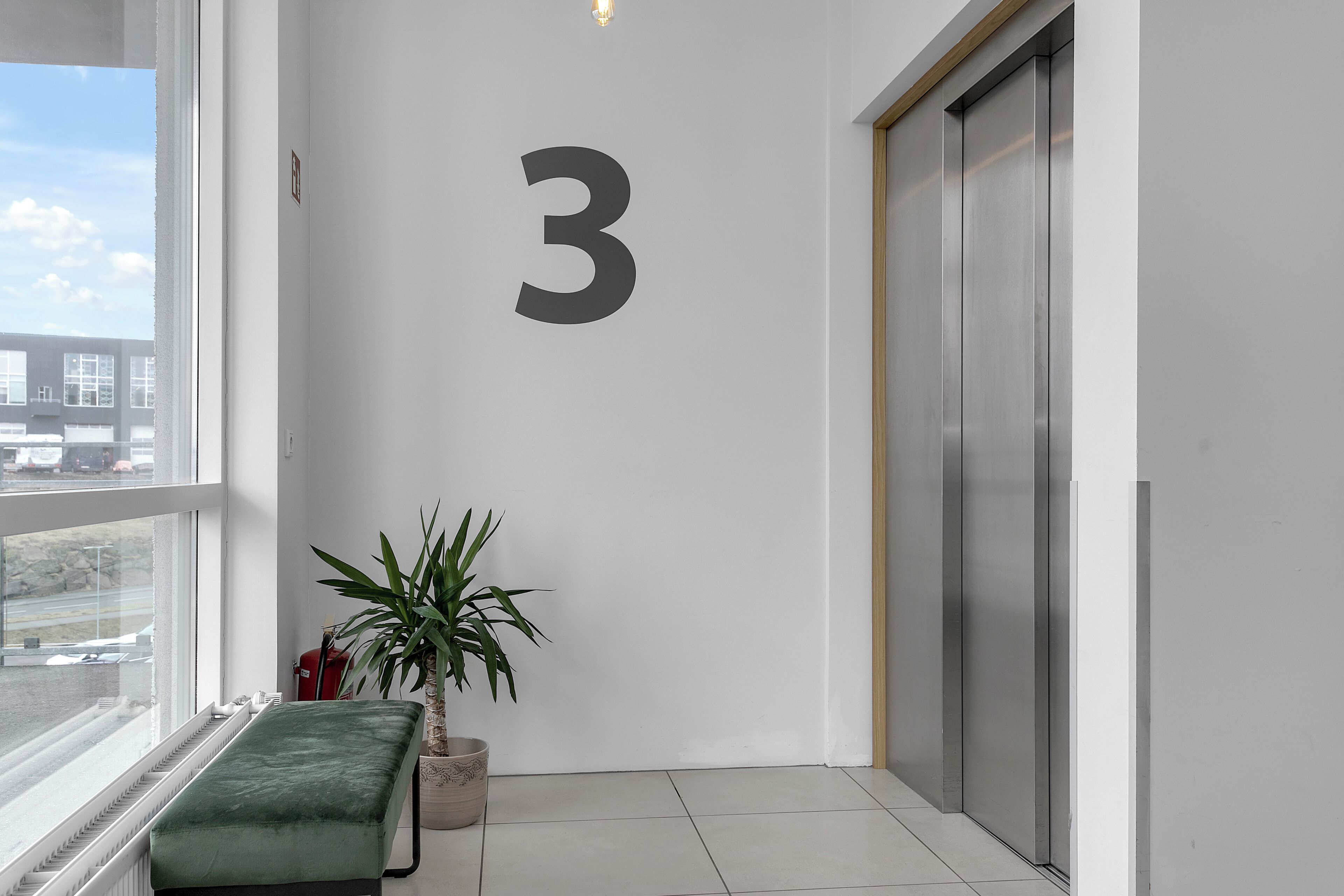 Un interior moderno con un gran número 3 en la pared, un banco, una planta en maceta y vistas al exterior a través de una ventana.