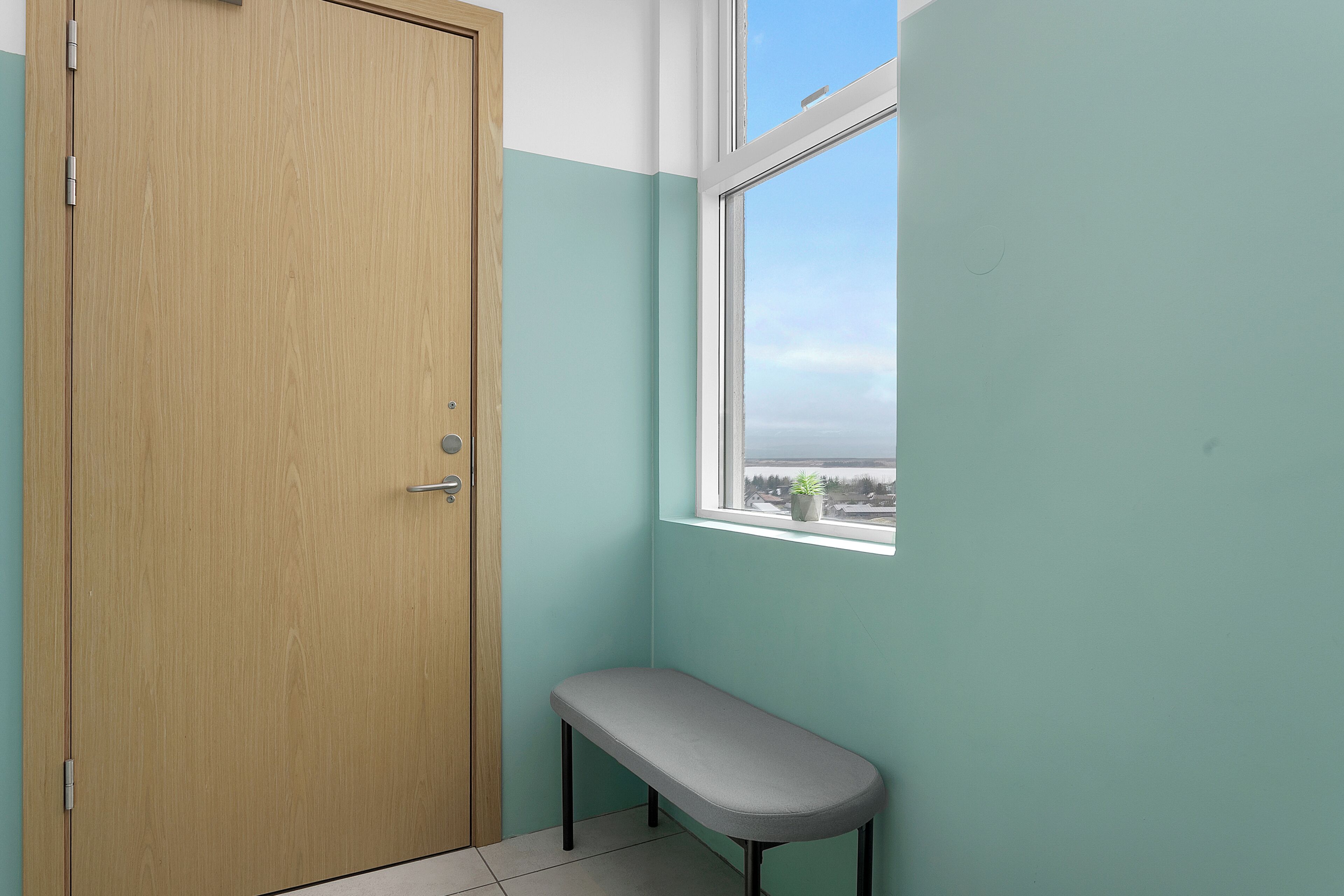 Un baño con puerta de madera, un banco y una ventana con vistas al exterior.