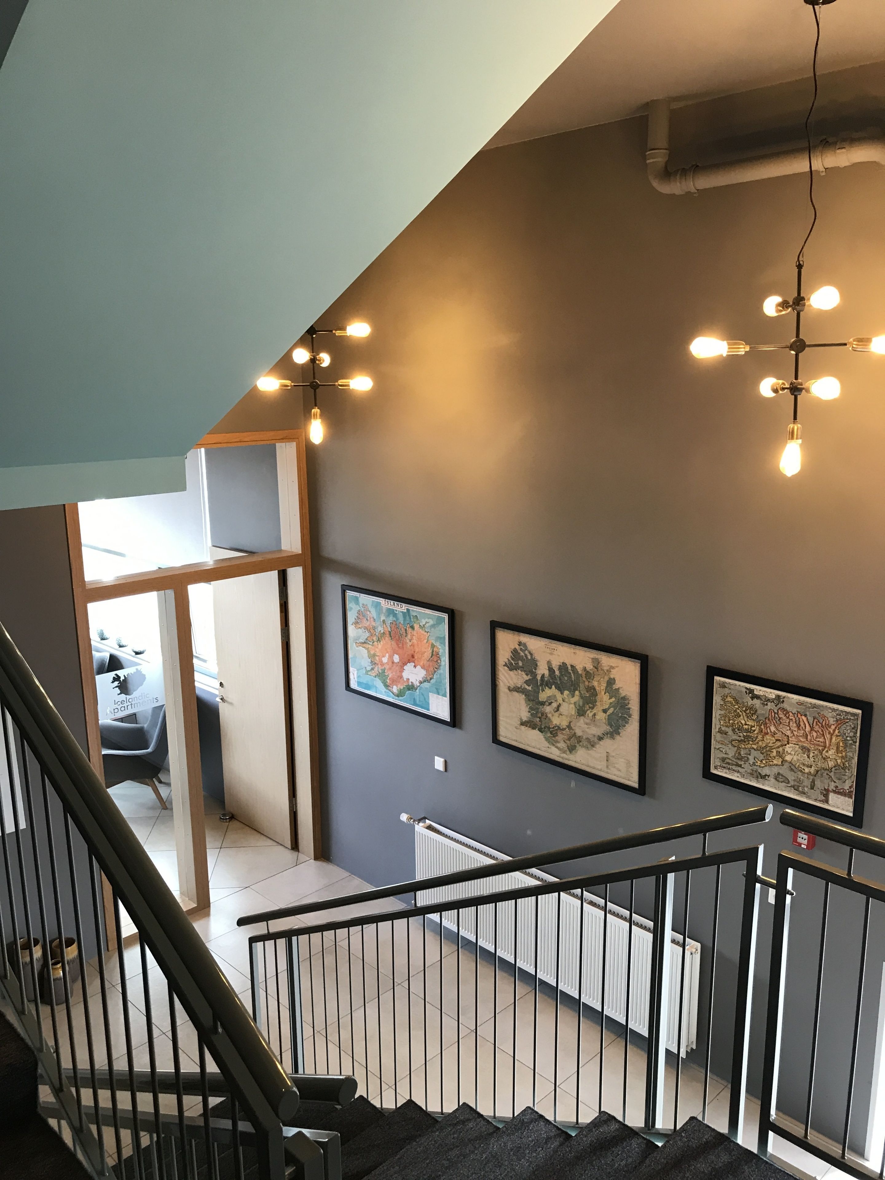 A staircase with a metal railing, a gray wall with framed artwork, and a ceiling light fixture.