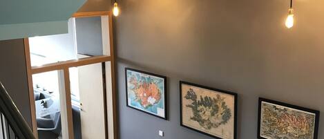 A staircase with a metal railing, a gray wall with framed artwork, and a ceiling light fixture.