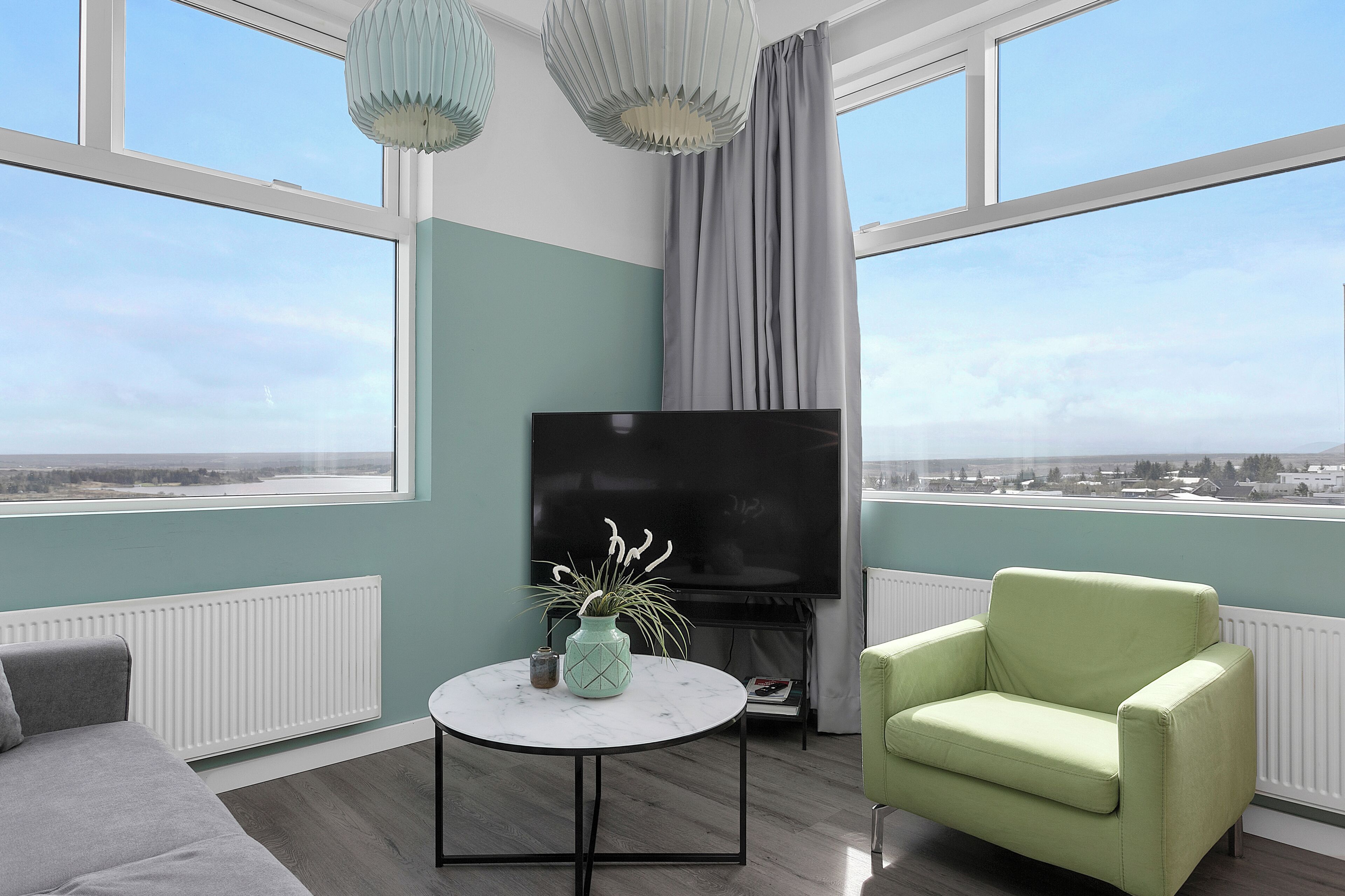 Un salon moderne avec une grande télévision, une table basse ronde et un fauteuil vert.