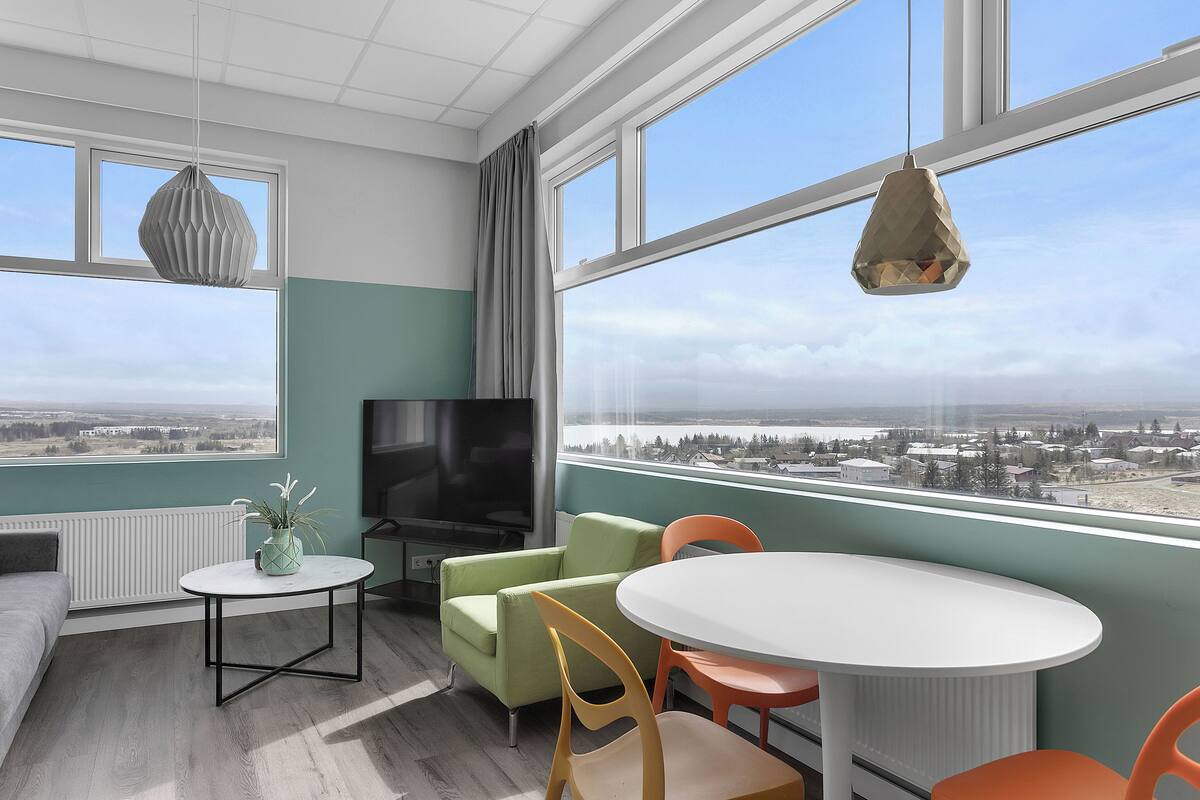 Une chambre moderne dotée d’une grande fenêtre, d’un téléviseur à écran plat, d’un canapé, d’une table à manger et de chaises.
