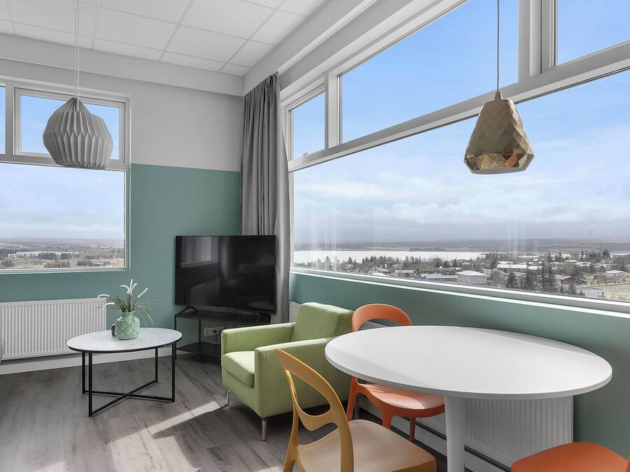 A modern room with a large window, a flat-screen TV, a sofa, a dining table, and chairs.