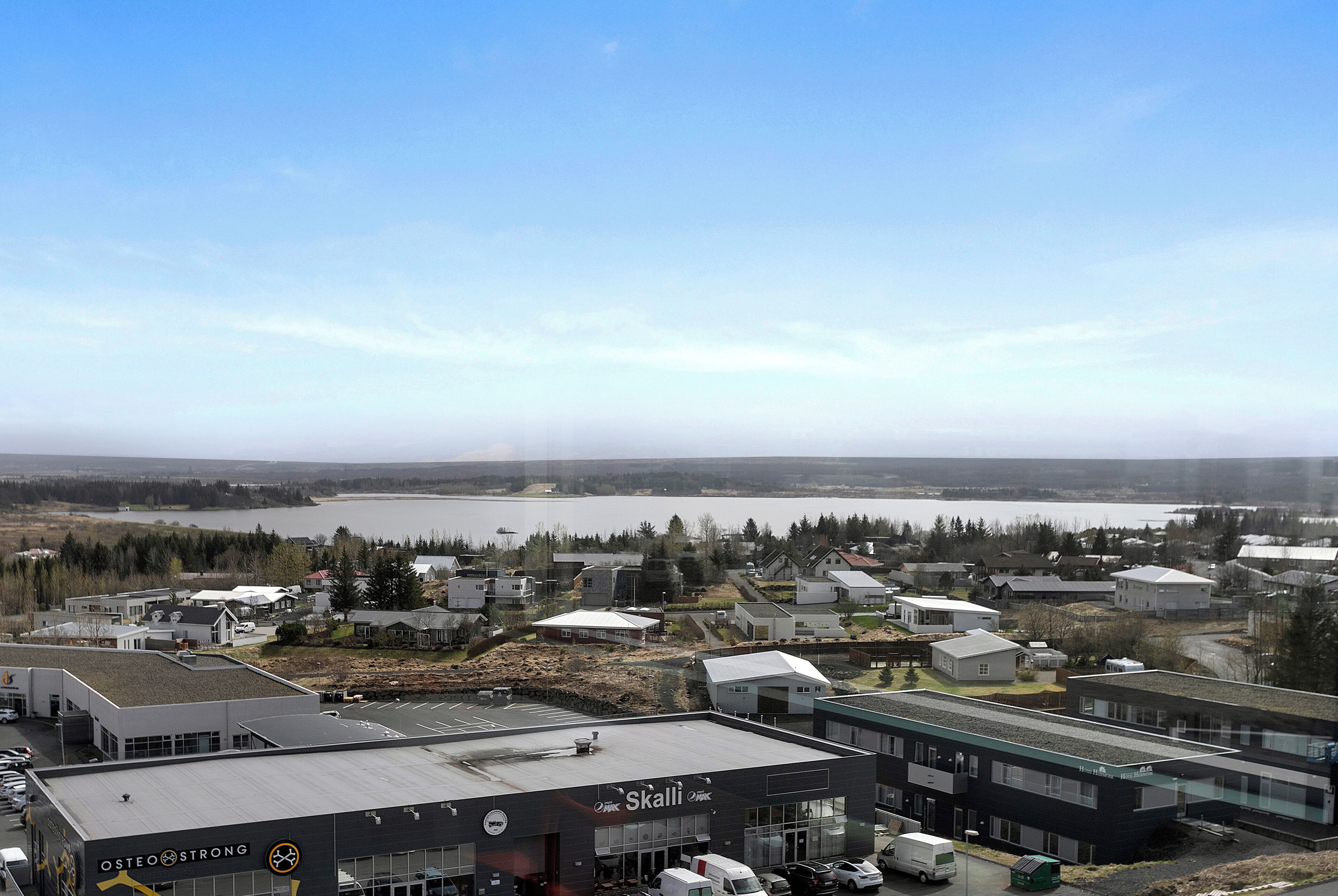 A commercial building with a parking lot and a view of a lake and residential area in the background.