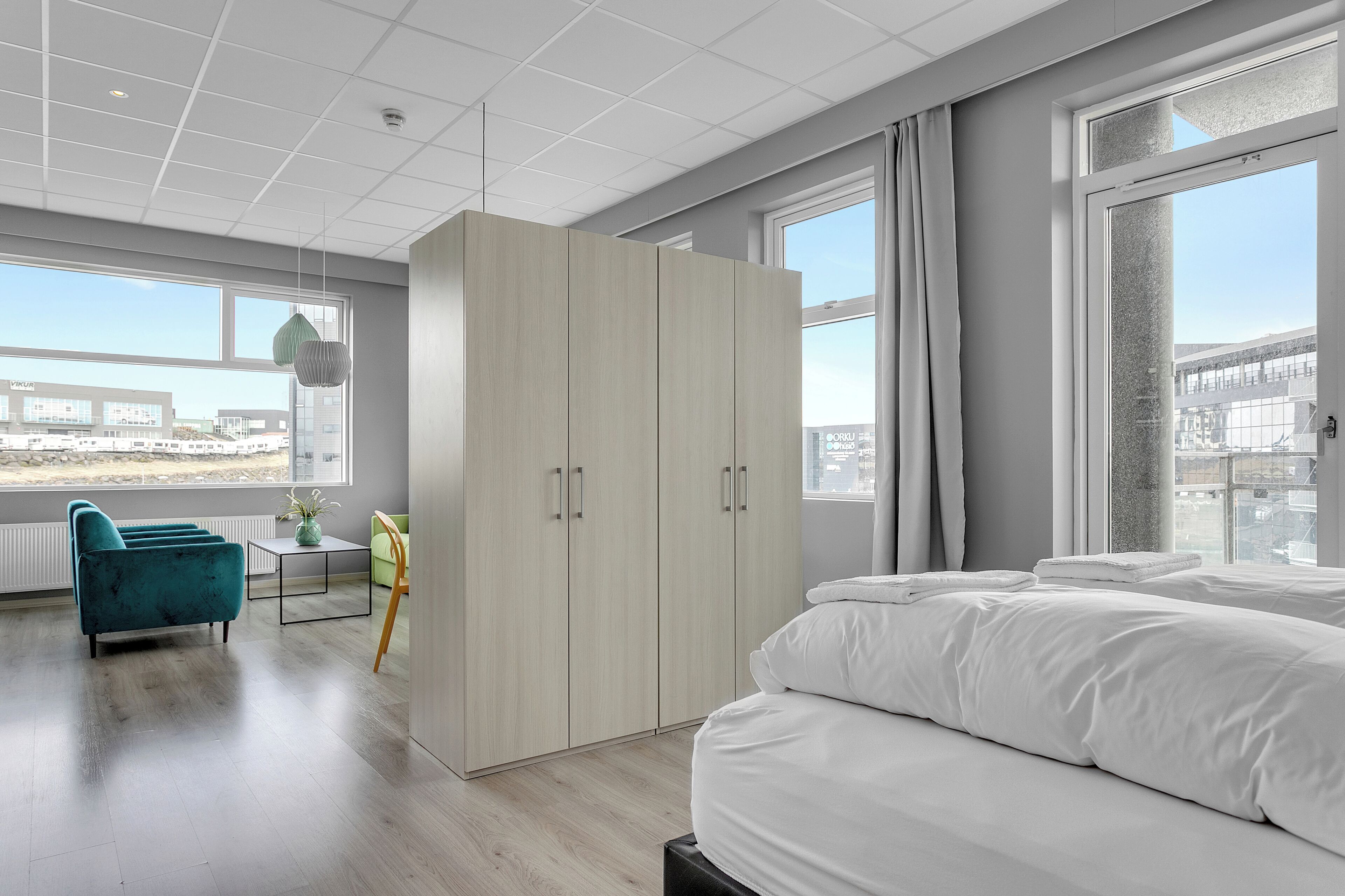 A modern hotel room with a large bed, a wardrobe, a desk, and a view of the city.