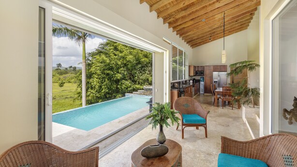 Un intérieur moderne avec une grande porte vitrée donnant sur une piscine, des meubles en osier et un coin cuisine.