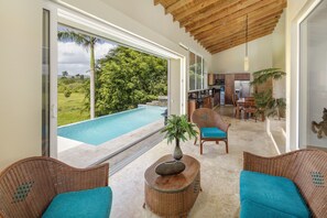 Un intérieur moderne avec une grande porte vitrée donnant sur une piscine, des meubles en osier et un coin cuisine.