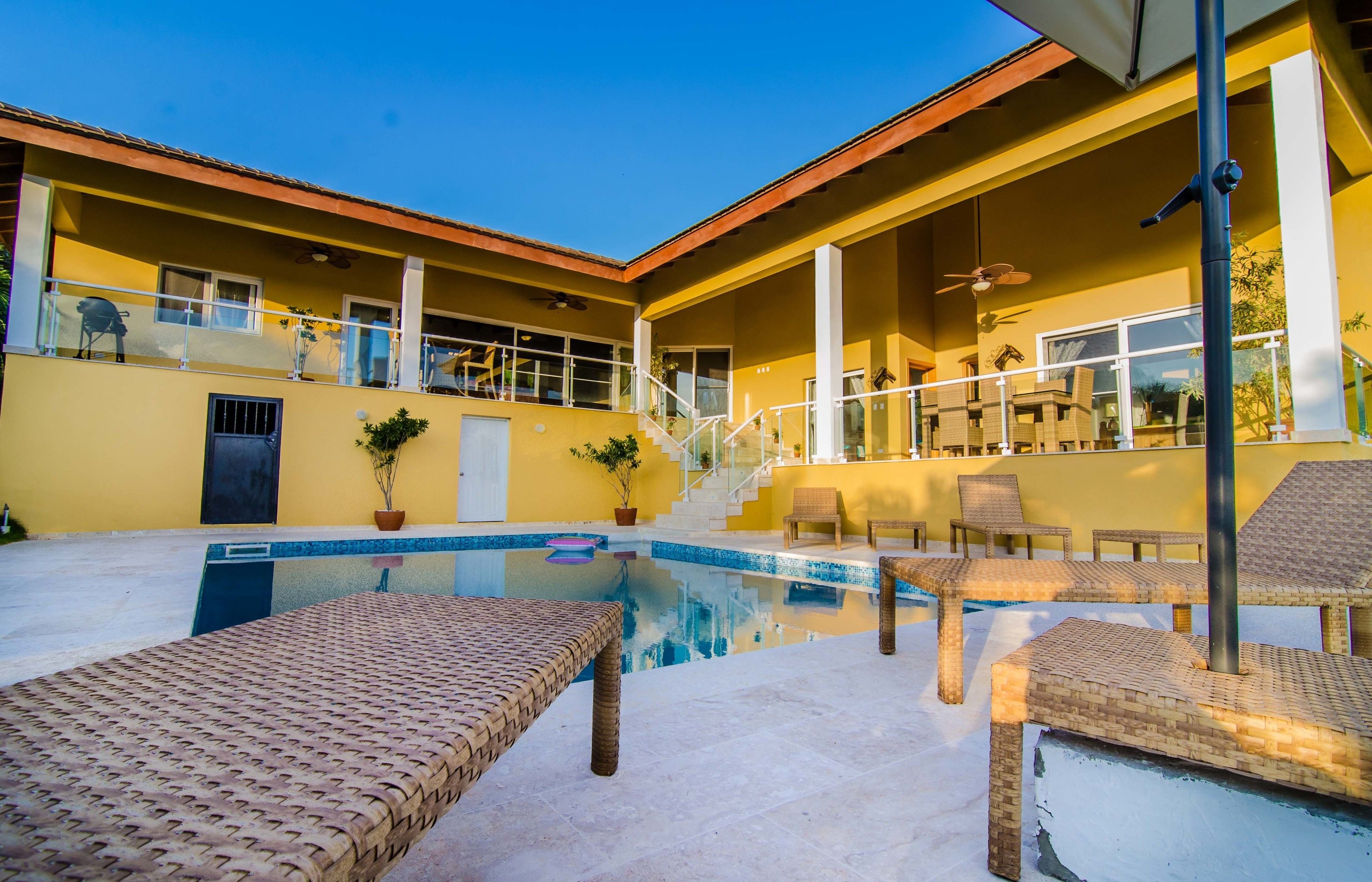 A pool area with lounge chairs and a staircase leading to a balcony.