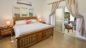 Une chambre avec un lit en bois, une table de chevet avec une lampe, une fenêtre donnant sur un beau paysage et une porte-fenêtre coulissante qui mène à un espace extérieur aménagé avec une table et des chaises.