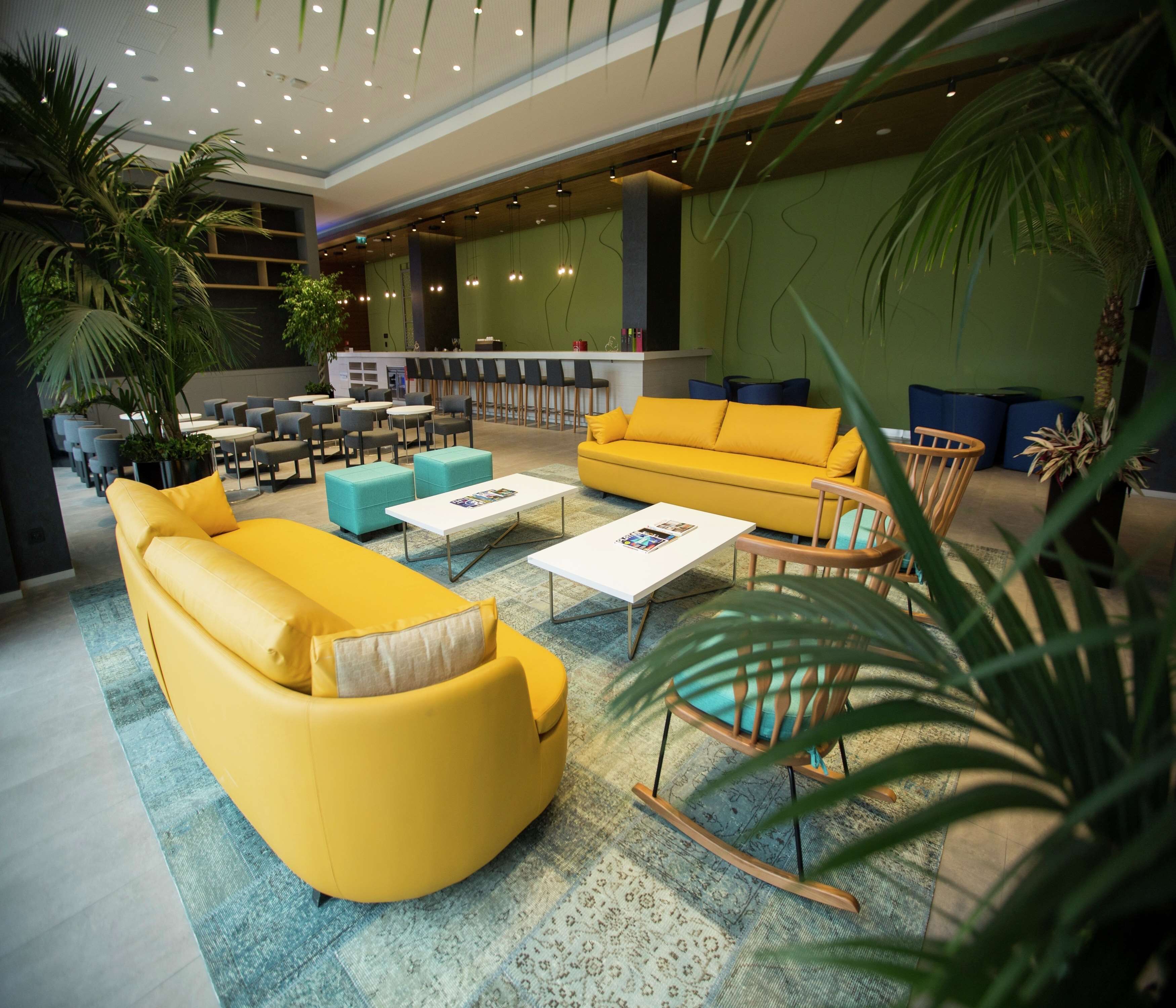 Un hall moderno con sofás amarillos, una mesa de centro y una zona de estar con sillas y mesas.