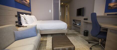 A hotel room with a bed, a sofa, a desk, a chair, and a television.