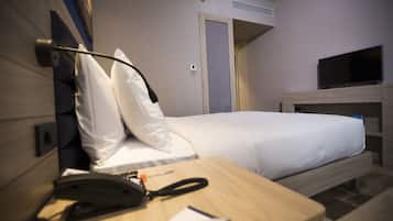 A hotel room with a bed, a desk with a telephone, a television on a stand, and a door leading to another room.
