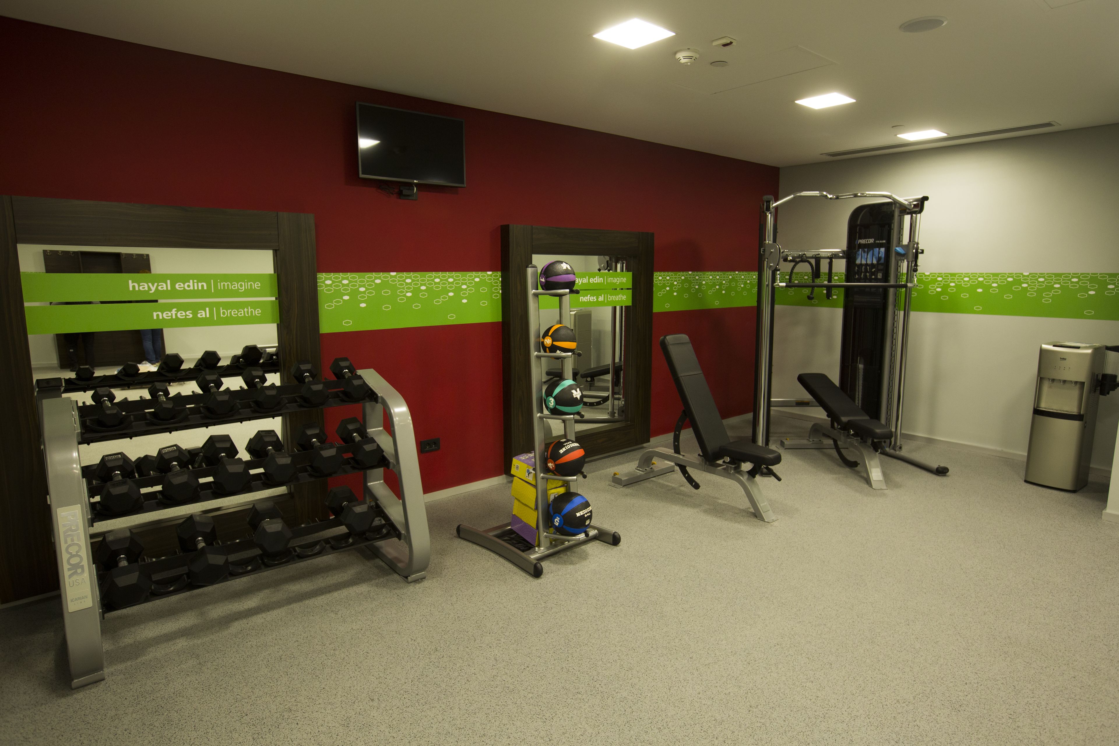 A gym with weightlifting equipment, a bench, and a TV on the wall.