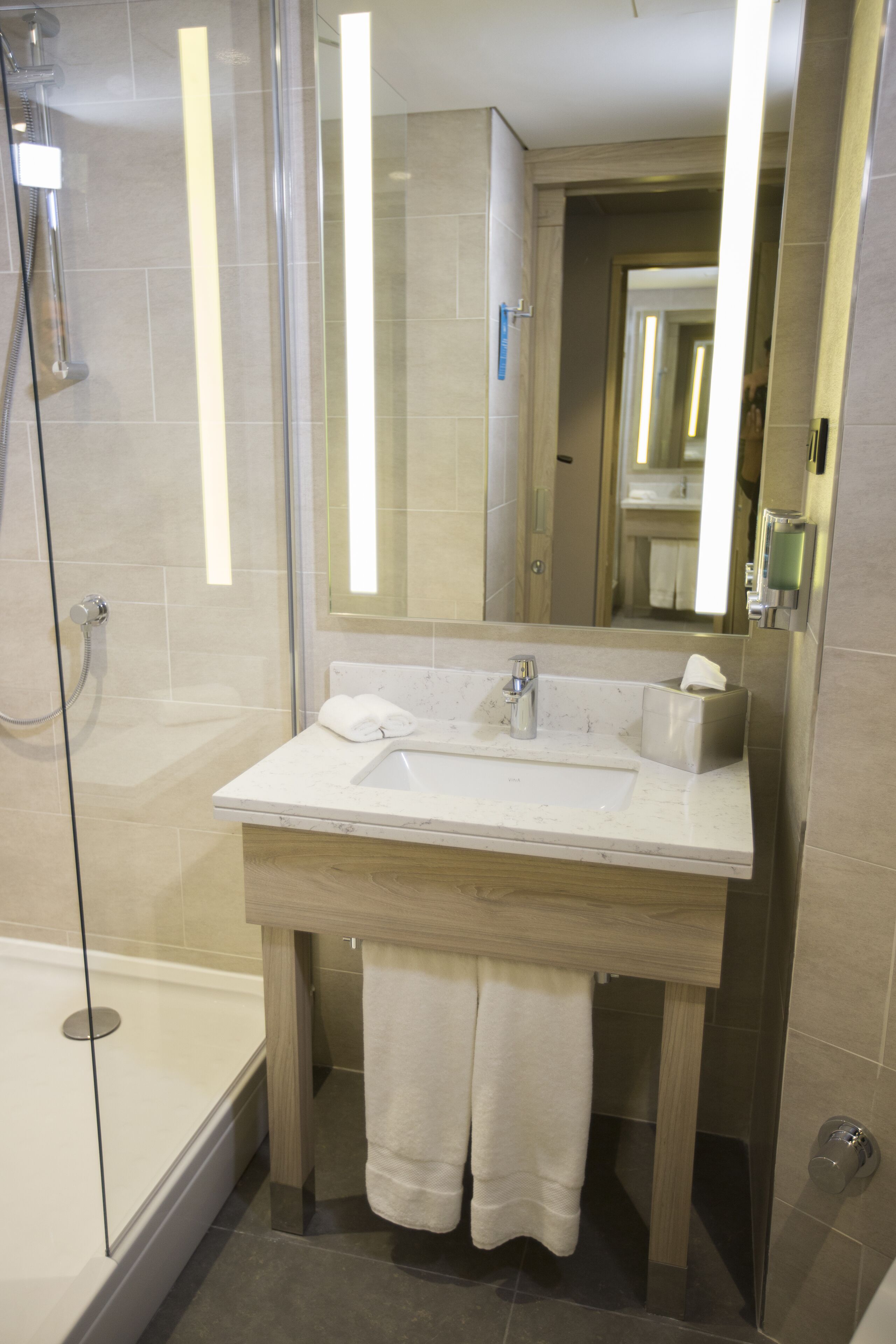 A modern bathroom with a glass-enclosed shower, a white sink, and a large mirror.