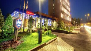 A hotel with a prominent 'Hampton' sign, a modern building with illuminated windows, and a well-lit entrance area with a flagpole and greenery. - Hampton by Hilton Bolu (Bolu)