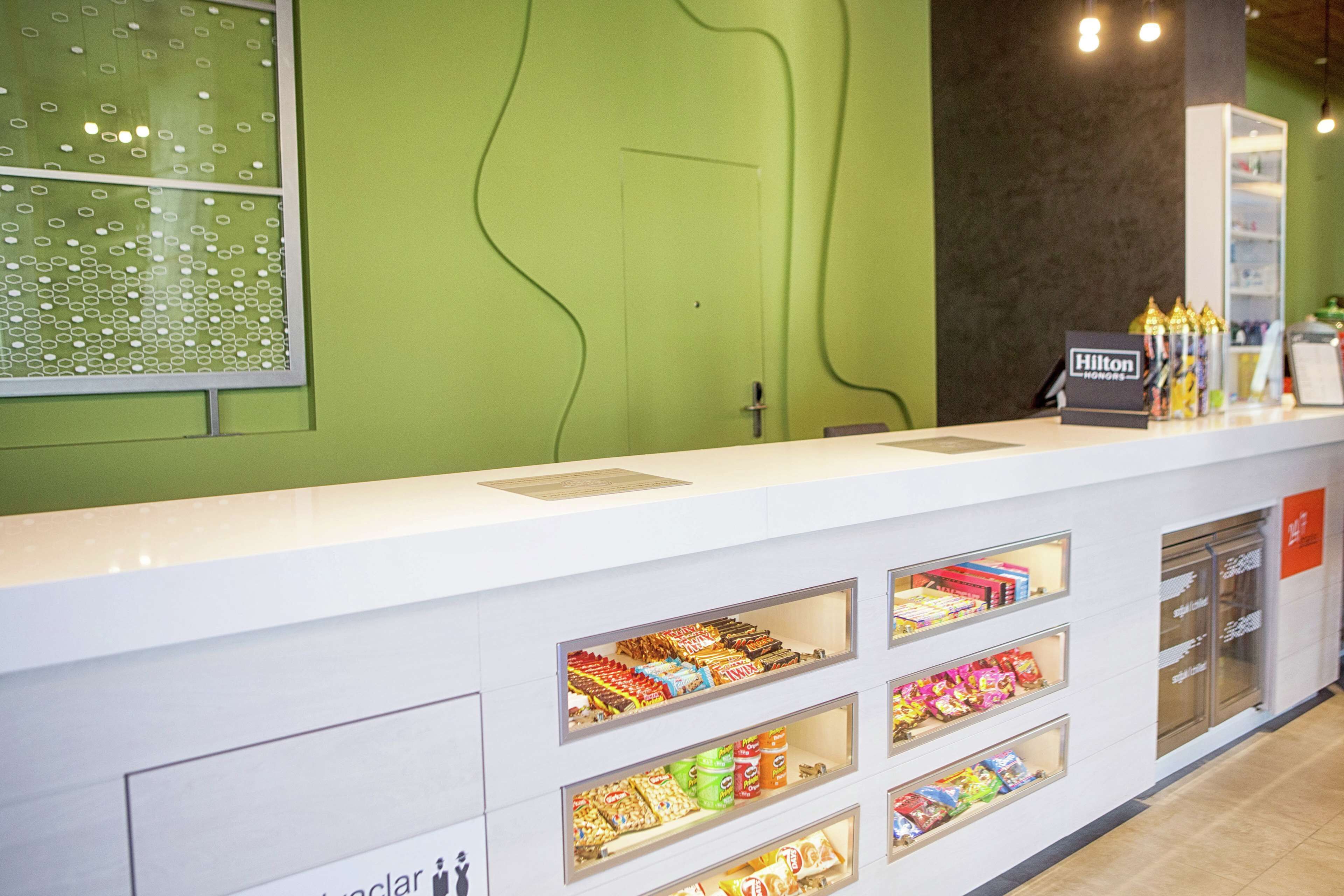 A hotel reception area with a green wall, a white reception desk, and multiple snack display cases.