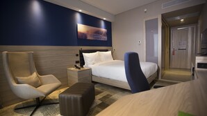A modern hotel room with a bed, two chairs, a nightstand, a flat-screen TV, and a wooden floor. - Hampton by Hilton Bolu (Bolu)