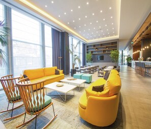 Un hall amplio con un sofá amarillo, sillas de balancín de madera y una zona de bar.