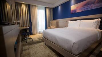 A hotel room with a large bed, a desk with a chair, a television, and a painting on the wall.