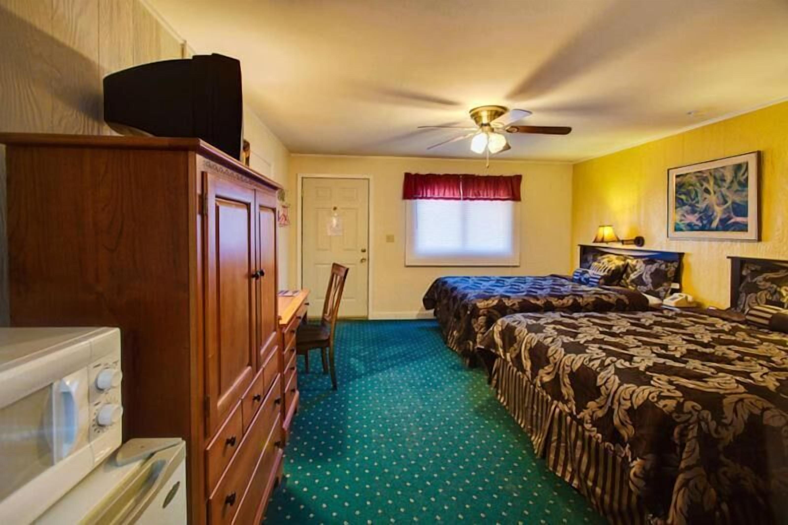 A bedroom with two beds, a ceiling fan, a window with red curtains, and a painting on the wall.