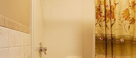 A shower with a floral curtain, a white towel, and a tiled wall.