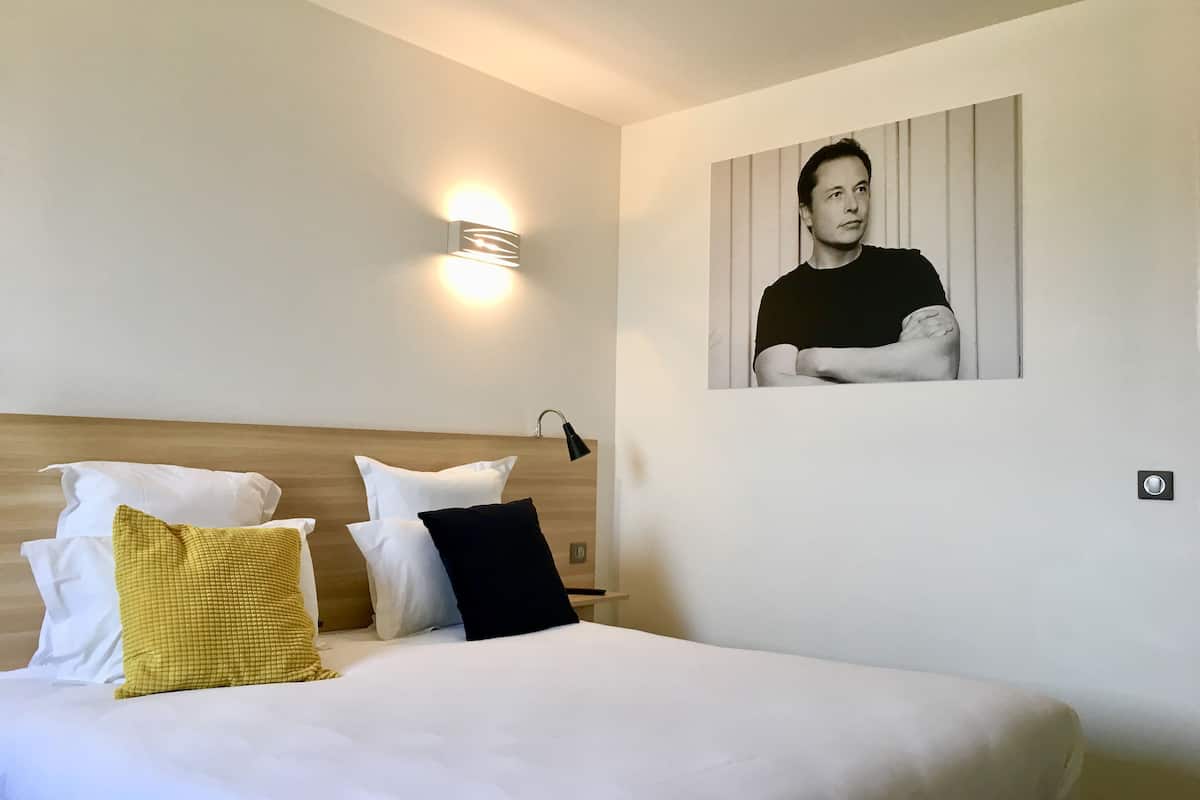 Una habitación de hotel con una cama bien hecha, un cuadro en la pared y una lámpara de noche.