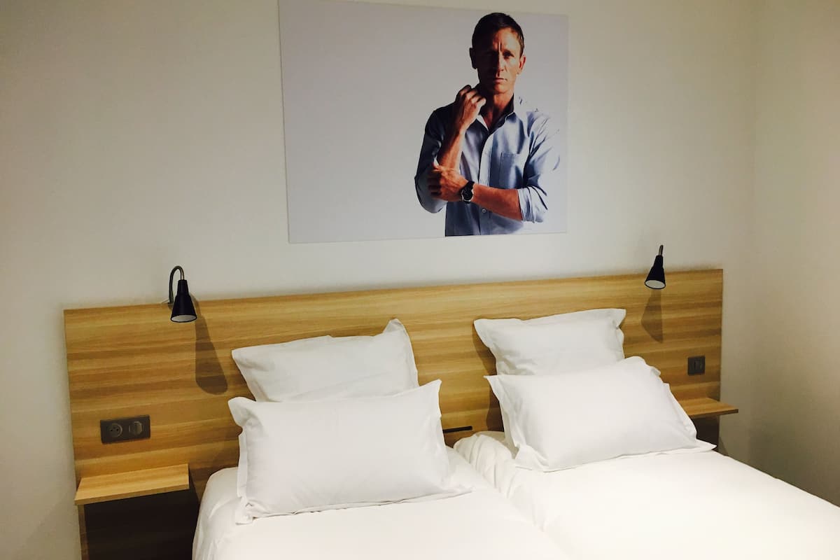 Habitación de hotel con cabecera de madera, dos almohadas blancas, una cama y un cuadro colgado en la pared de un hombre con camisa azul.